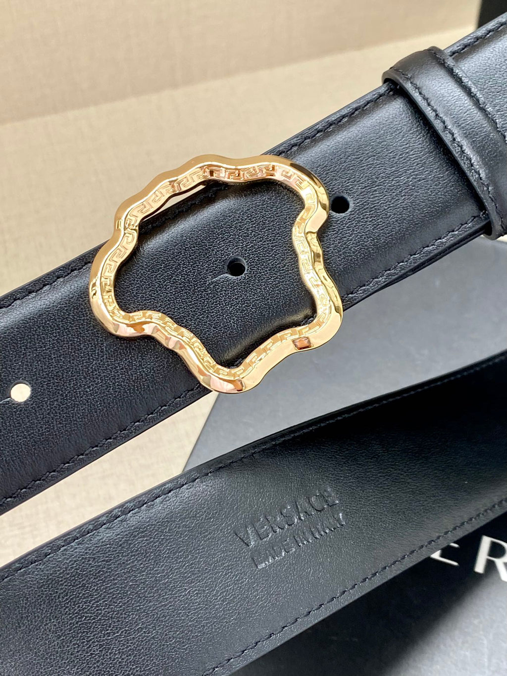 Dark leather belt with gold-tone ornate buckle and embossed branding