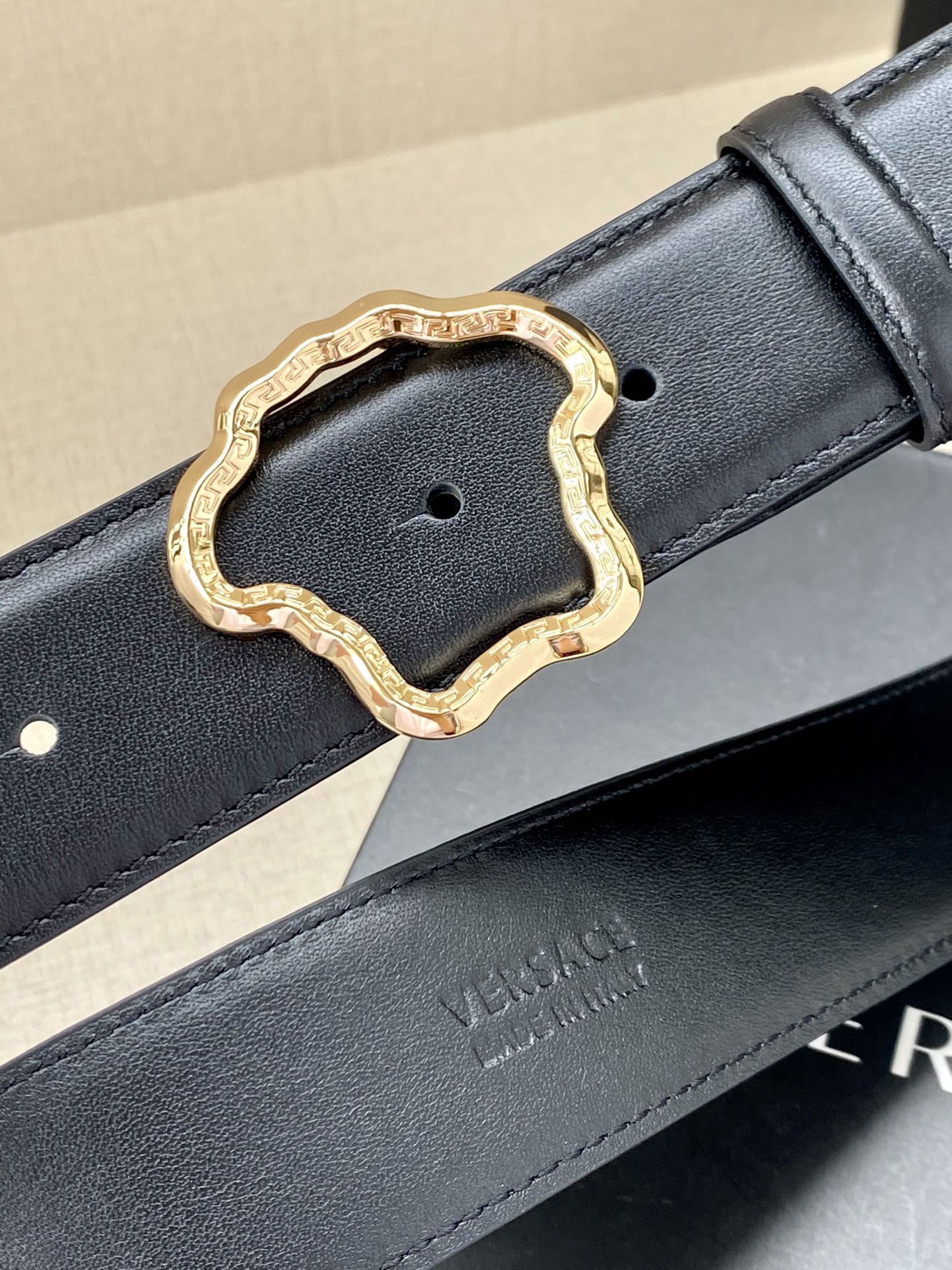 Dark leather belt with gold-tone ornate buckle and embossed branding
