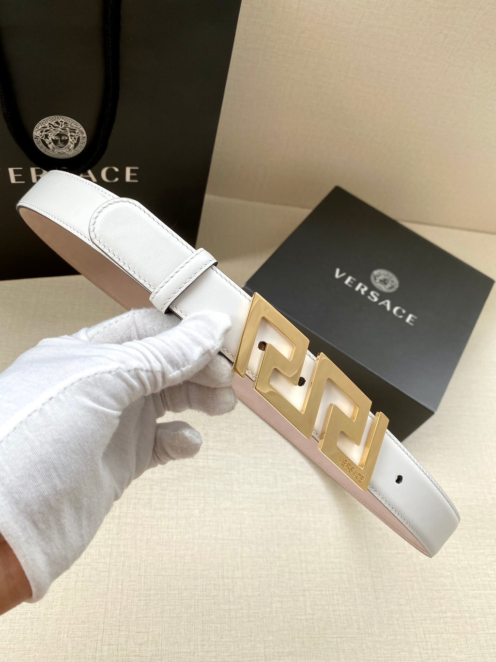 White leather belt with gold-tone FF buckle, held by gloved hand