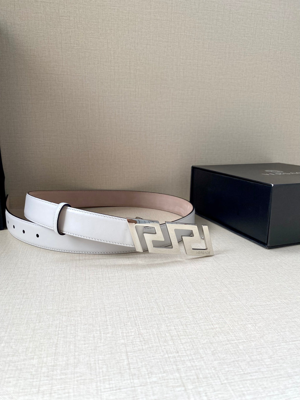 White leather belt with gold-tone FF buckle, belt looped on a surface