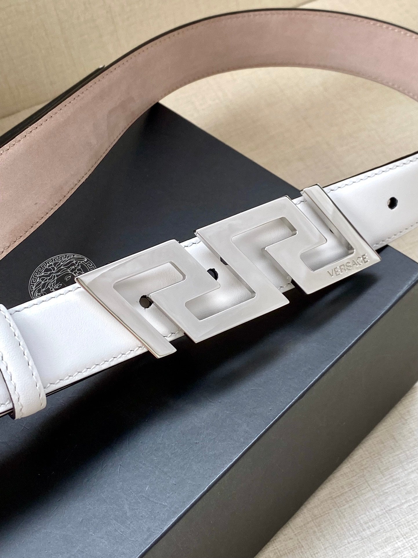 White leather belt close-up with silver-tone FF buckle and logo plate