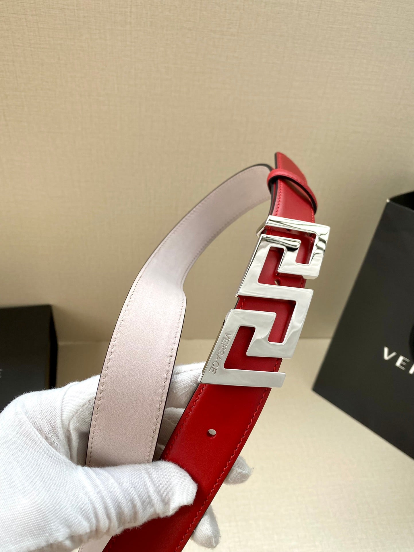 Versace belt with light pink strap, red keeper panel, and gold Greek-key buckle