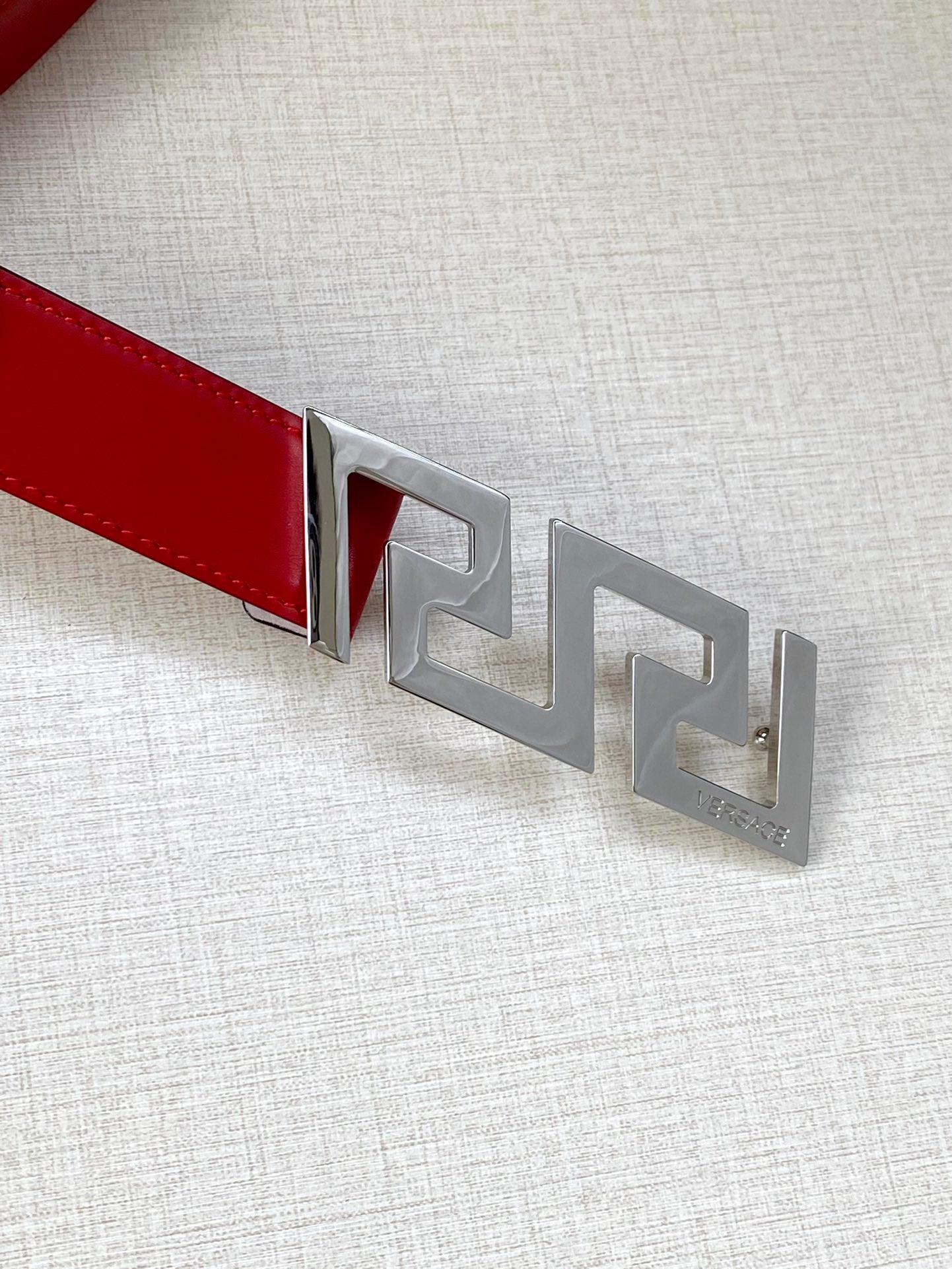 Versace belt close-up: red leather strap with silver Greek-key buckle