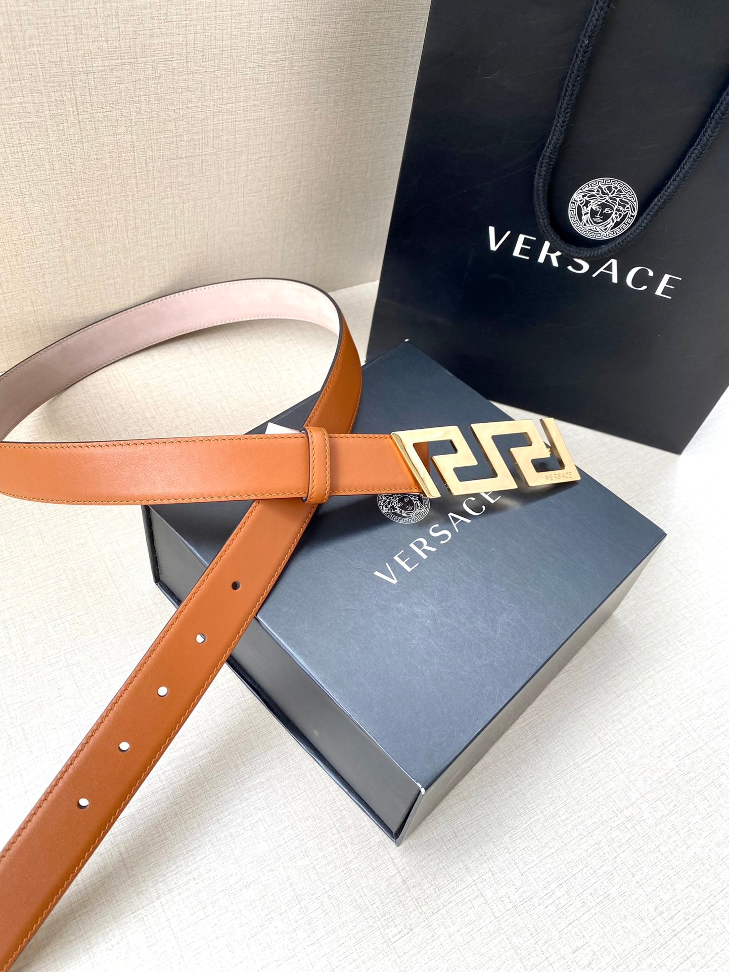 Orange leather belt with gold-tone logo buckle and multiple adjustment holes.