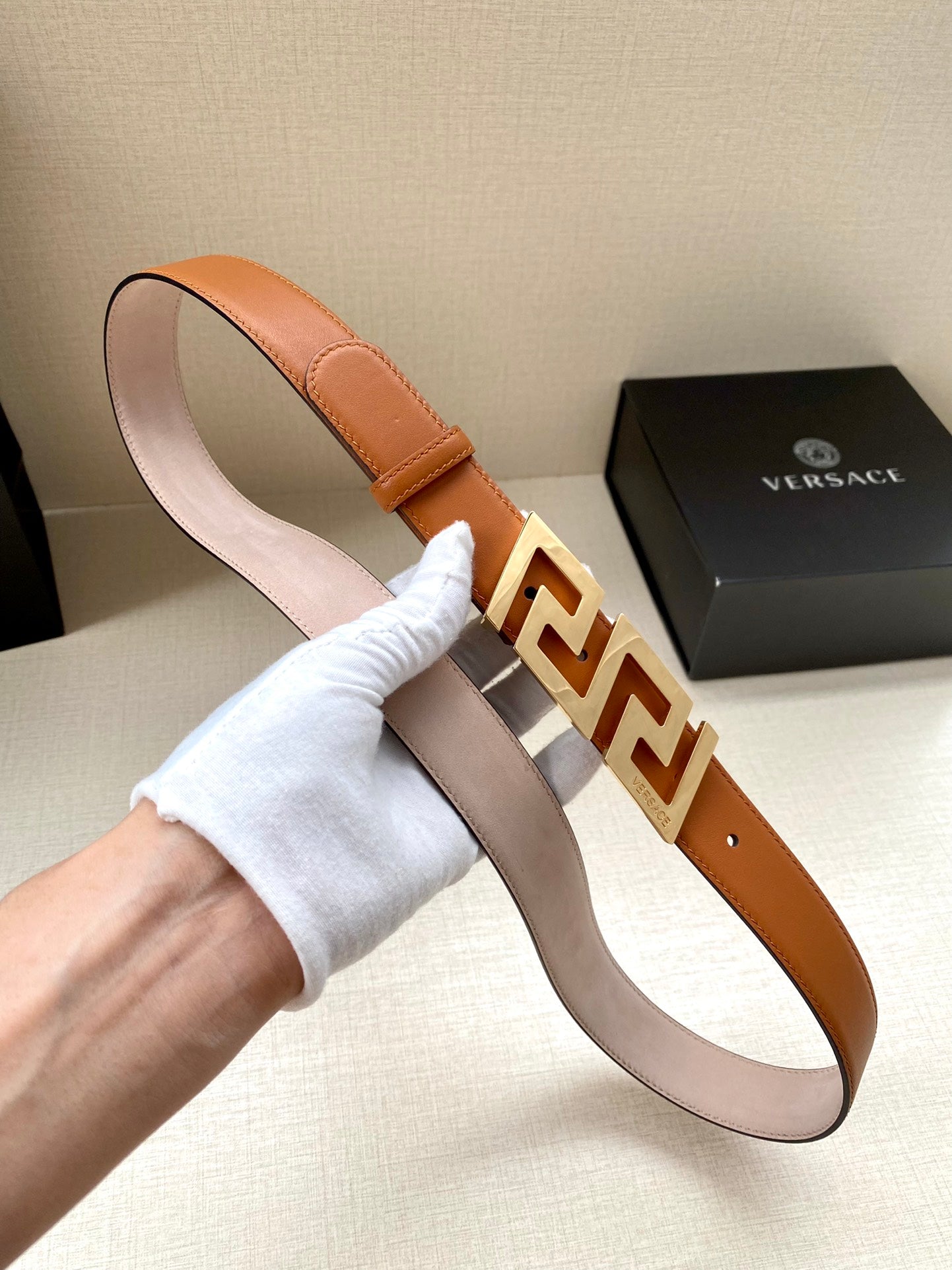 Orange leather belt with silver-tone logo buckle and stitched edge, held upright.