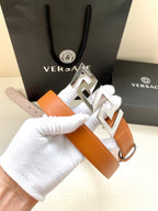 Orange leather belt with silver-tone logo buckle, shown close-up on a hand.