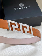 Tan leather belt with large silver-tone logo buckle and square pin holes.