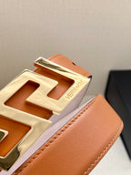 Close-up of orange leather belt edge and gold-tone logo buckle with embossed detail.