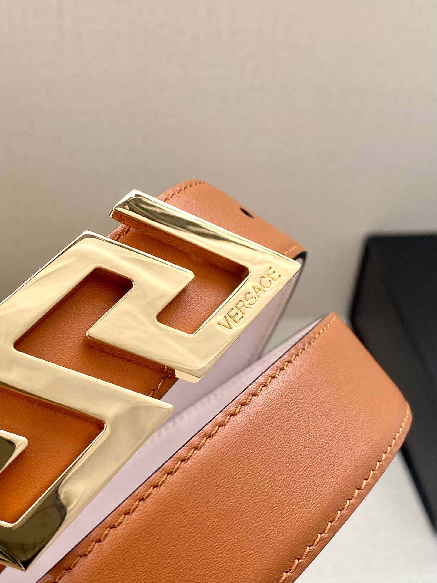 Close-up of orange leather belt edge and gold-tone logo buckle with embossed detail.