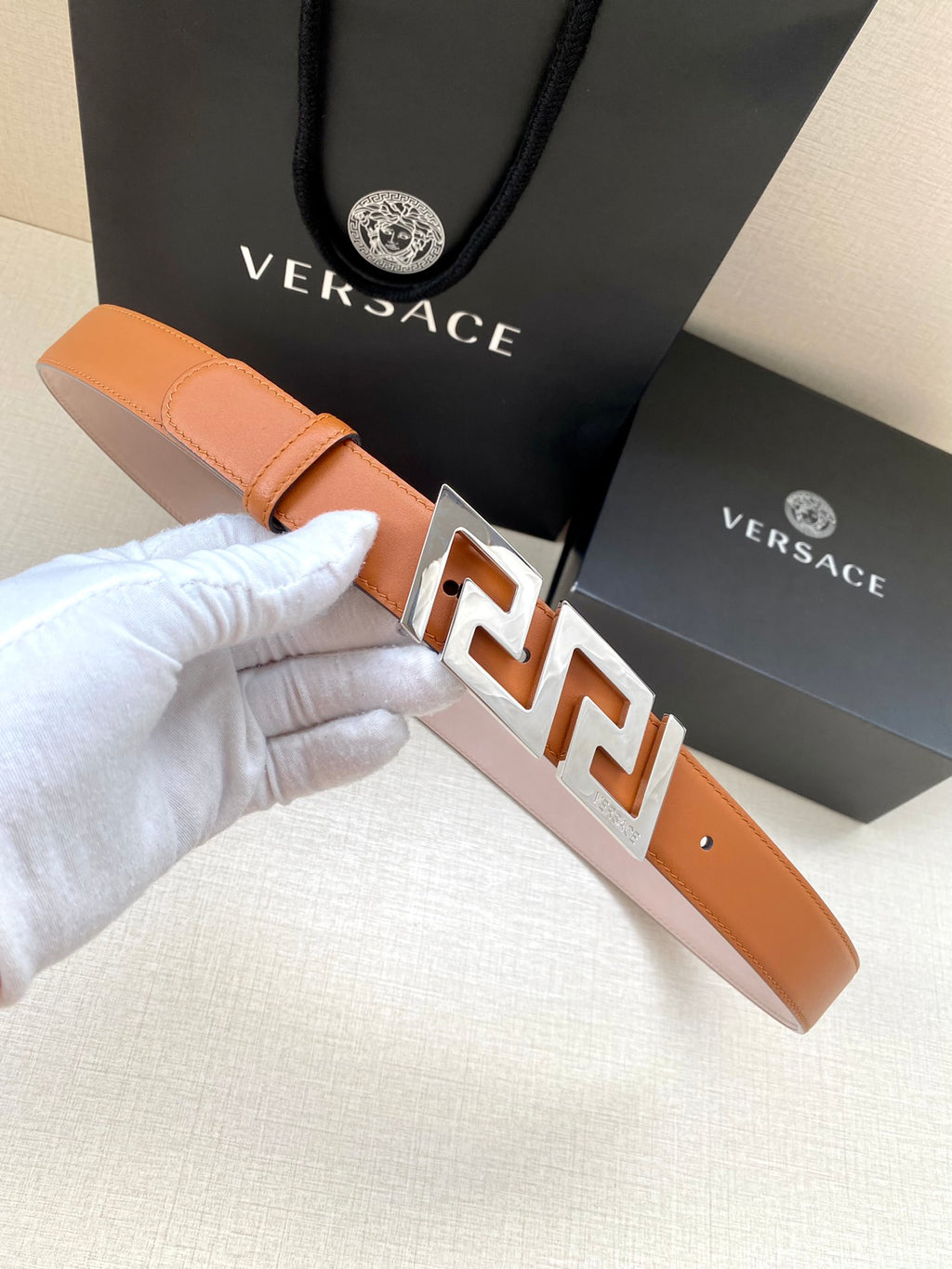 Orange leather belt with silver-tone buckle featuring interlocking logo design.