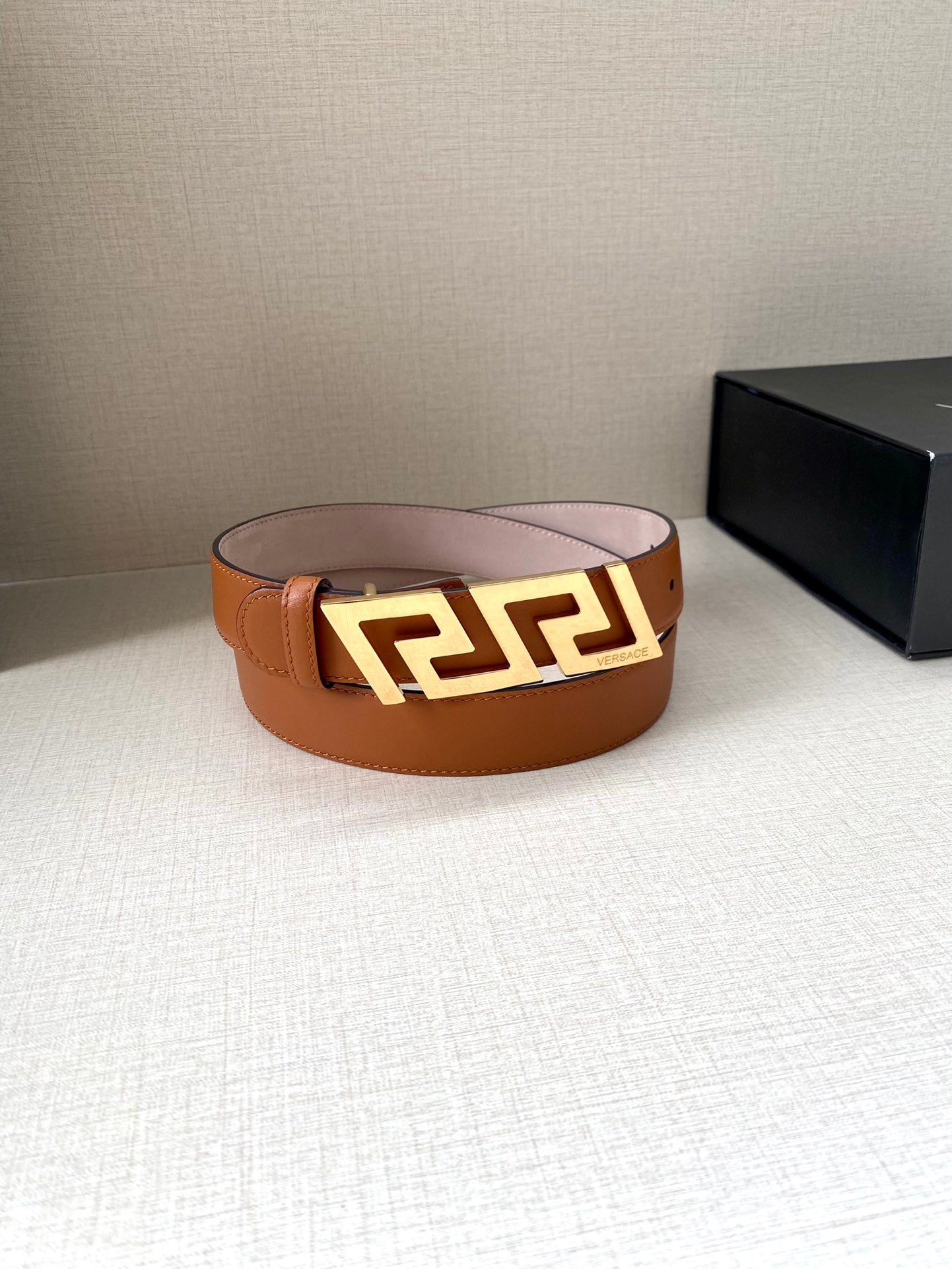 Orange leather belt with gold-tone buckle and logo motif; flat front view.