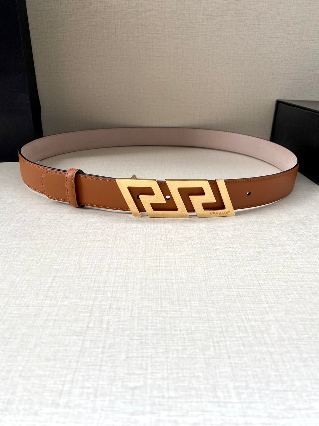 Orange leather belt with gold-tone logo buckle centered across the strap.