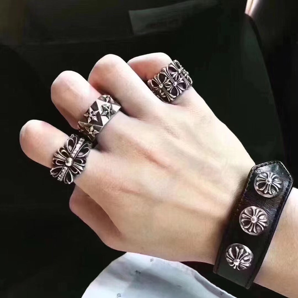 Silver-tone floral rings and black leather cuff bracelet on hand.
