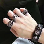 Silver-tone floral rings and black leather cuff bracelet on hand.