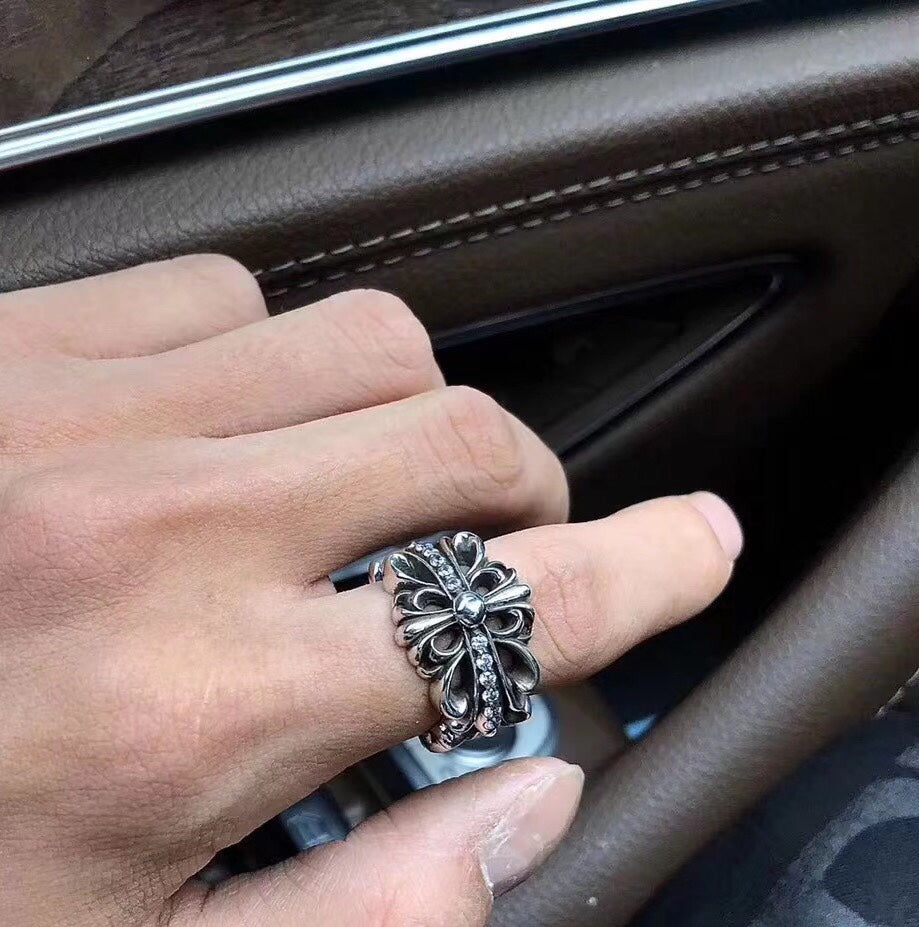 Silver-tone floral cross ring on finger, blackened metal finish.