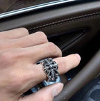 Silver-tone floral cross ring on finger, blackened metal finish.