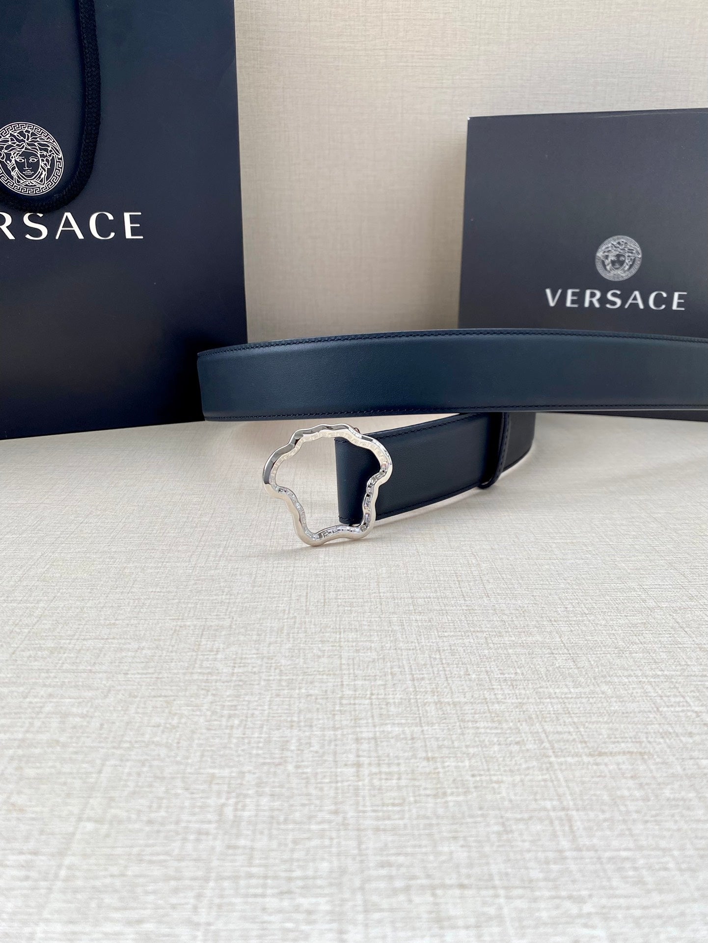 Dark blue leather belt with silver-tone logo buckle, centered on tabletop