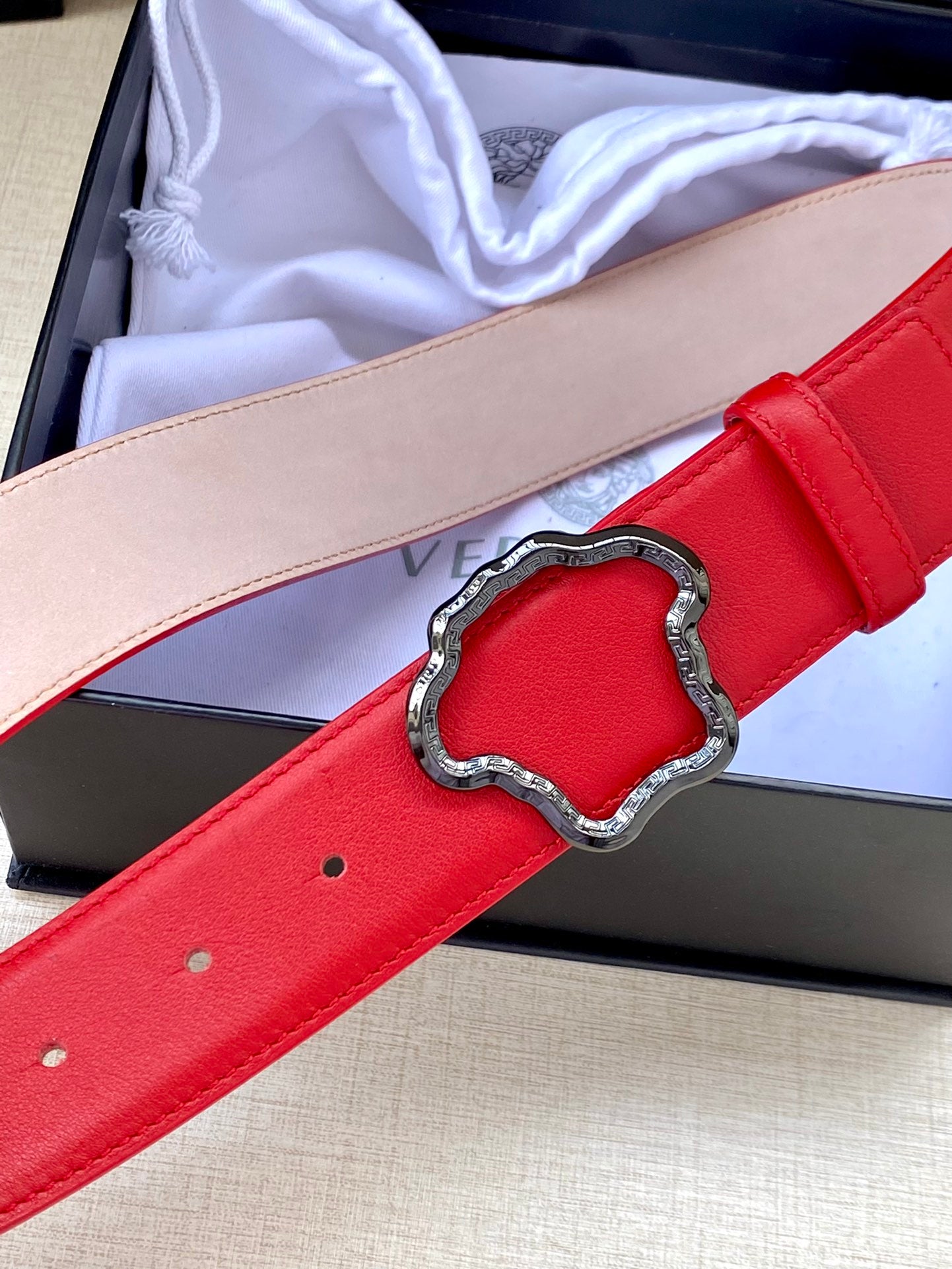 Red leather belt with silver Medusa-style buckle, close-up with punched holes