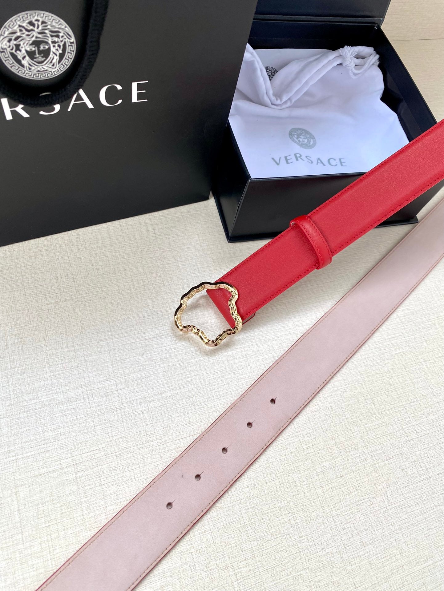 Red leather belt with gold Medusa-style buckle and pale pink reverse strap