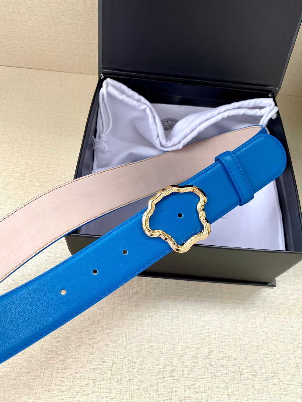 Versace belt in bright blue leather partially inside box, with gold-toned buckle