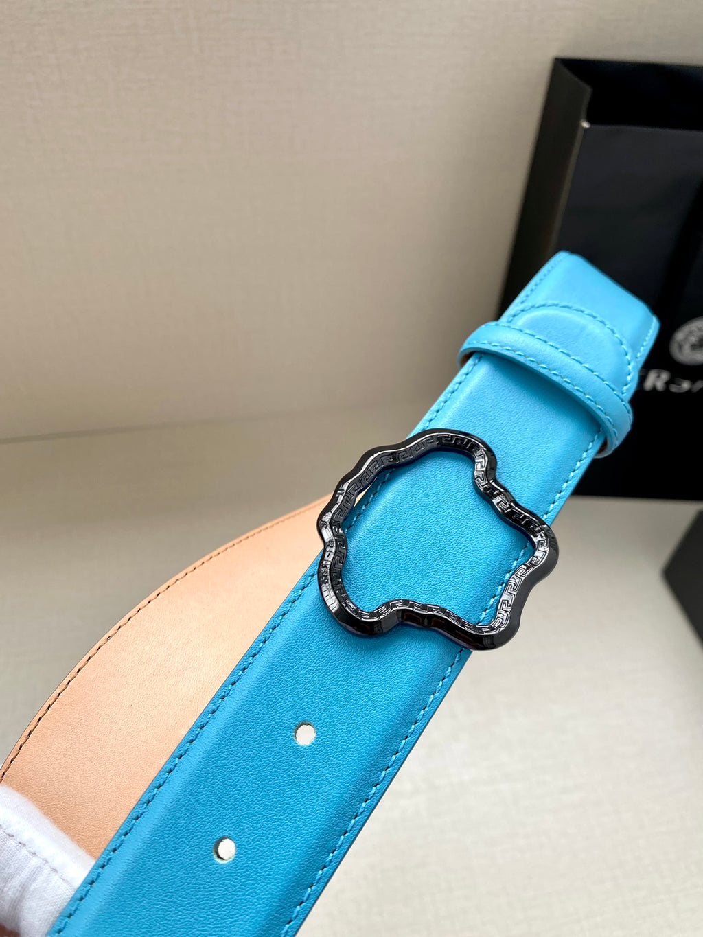 Blue leather belt close-up: buckle set on strap with two punched holes.