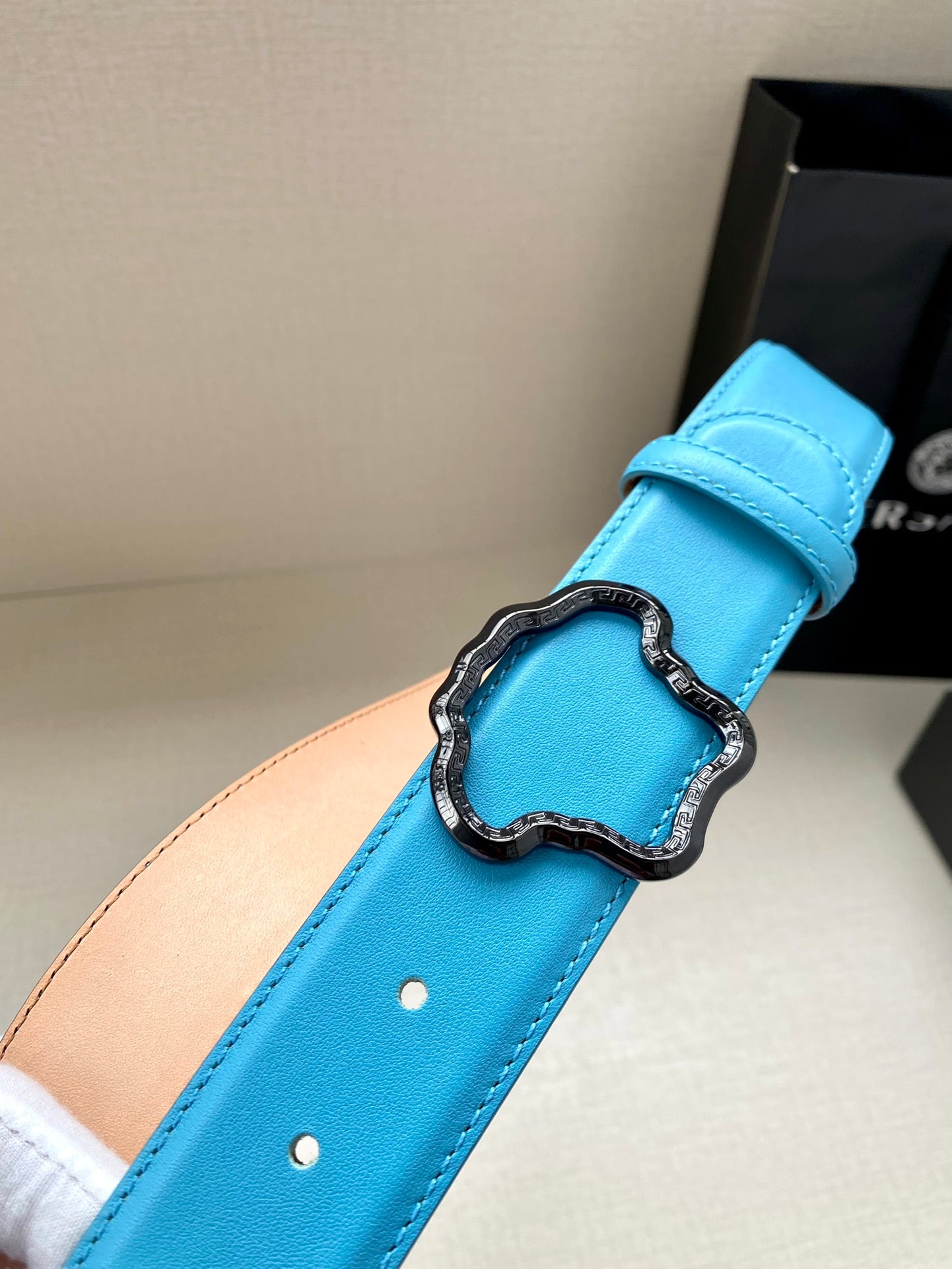 Blue leather belt close-up: buckle set on strap with two punched holes.