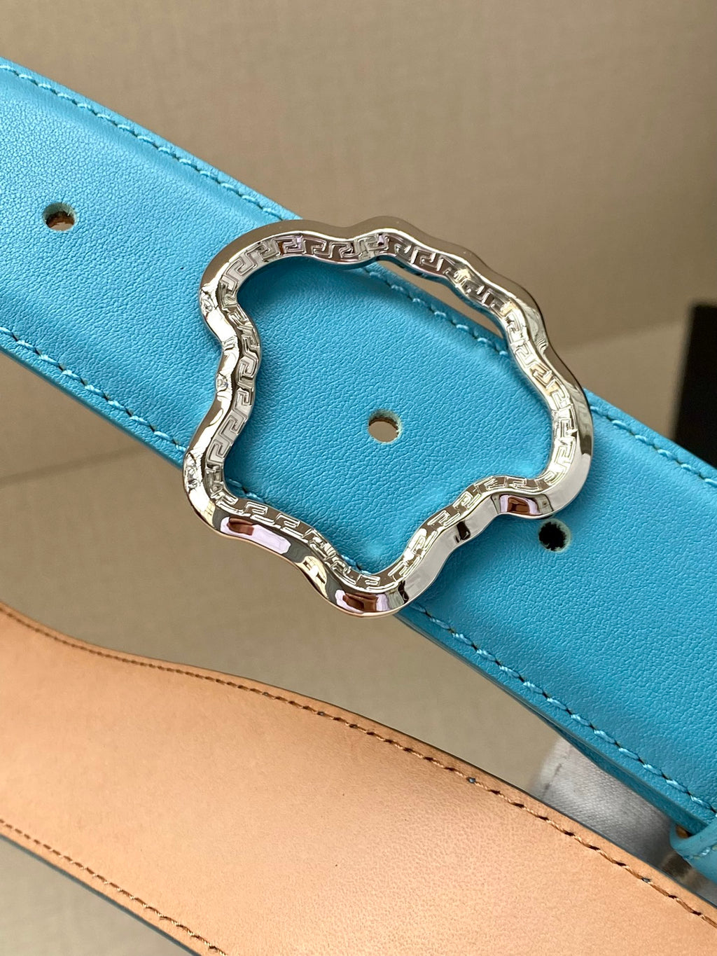 Blue leather belt close-up: ornate buckle with cutout center and stitching.