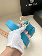 Blue leather belt with gold-toned ornate buckle and strap held in gloved hand.