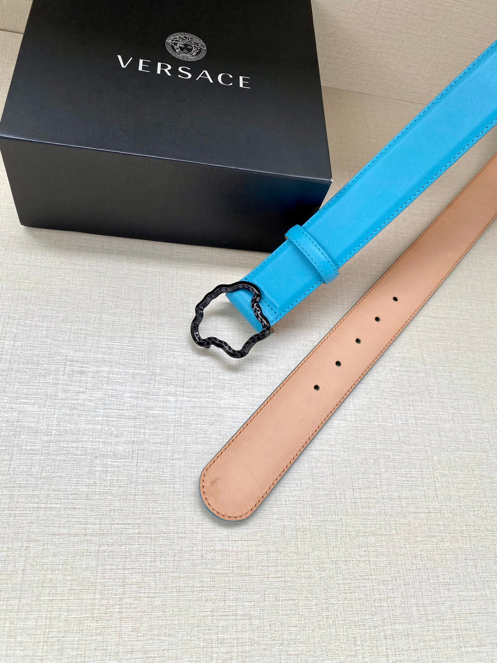 Blue leather belt with center buckle; tan underside visible and stitched edge.