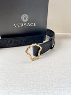 Versace belt buckle close-up, dark navy with embossed logo pattern and gold-tone frame.