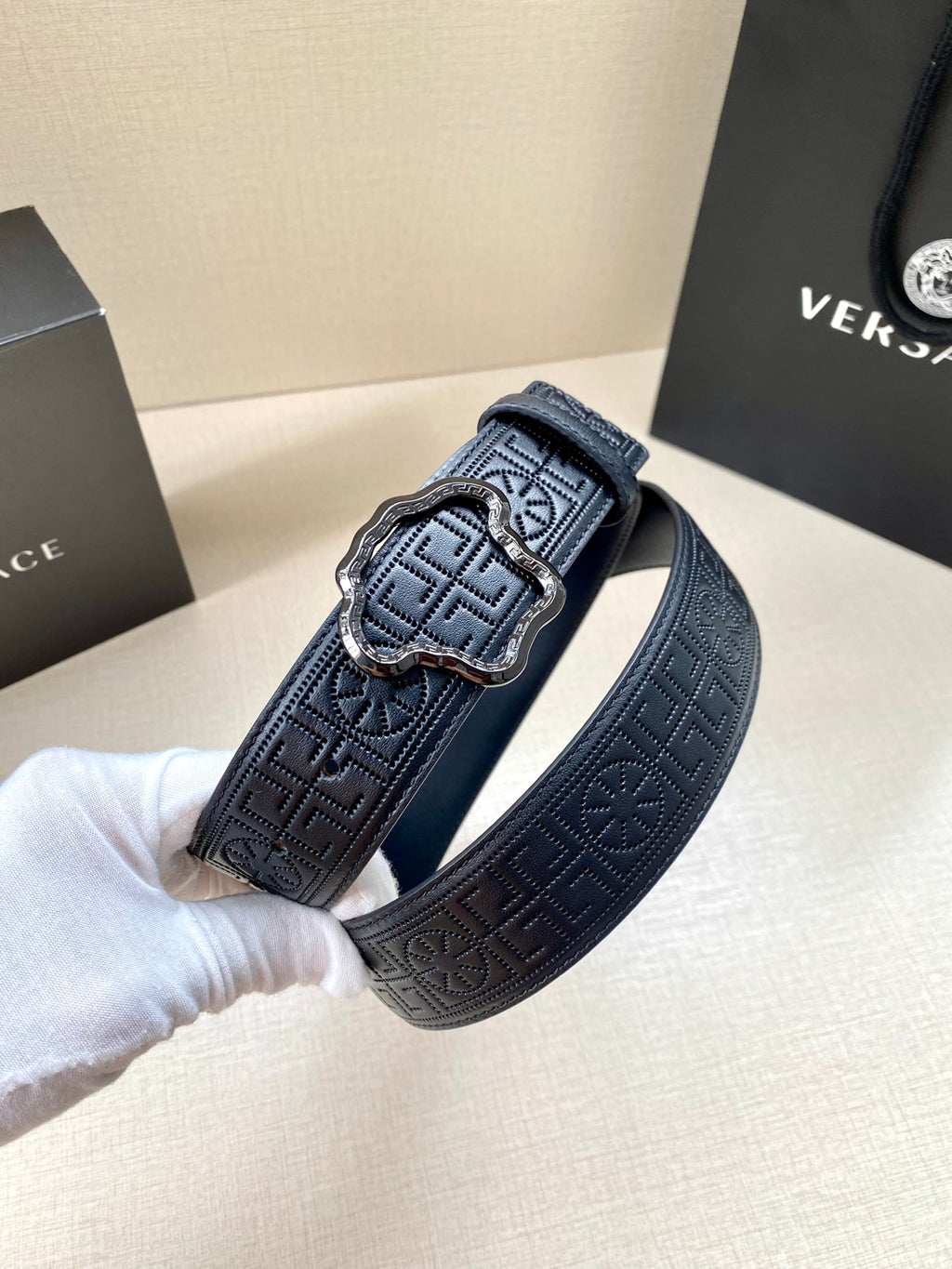 Versace belt close-up, dark navy logo texture and rectangular buckle with gold-tone accents.