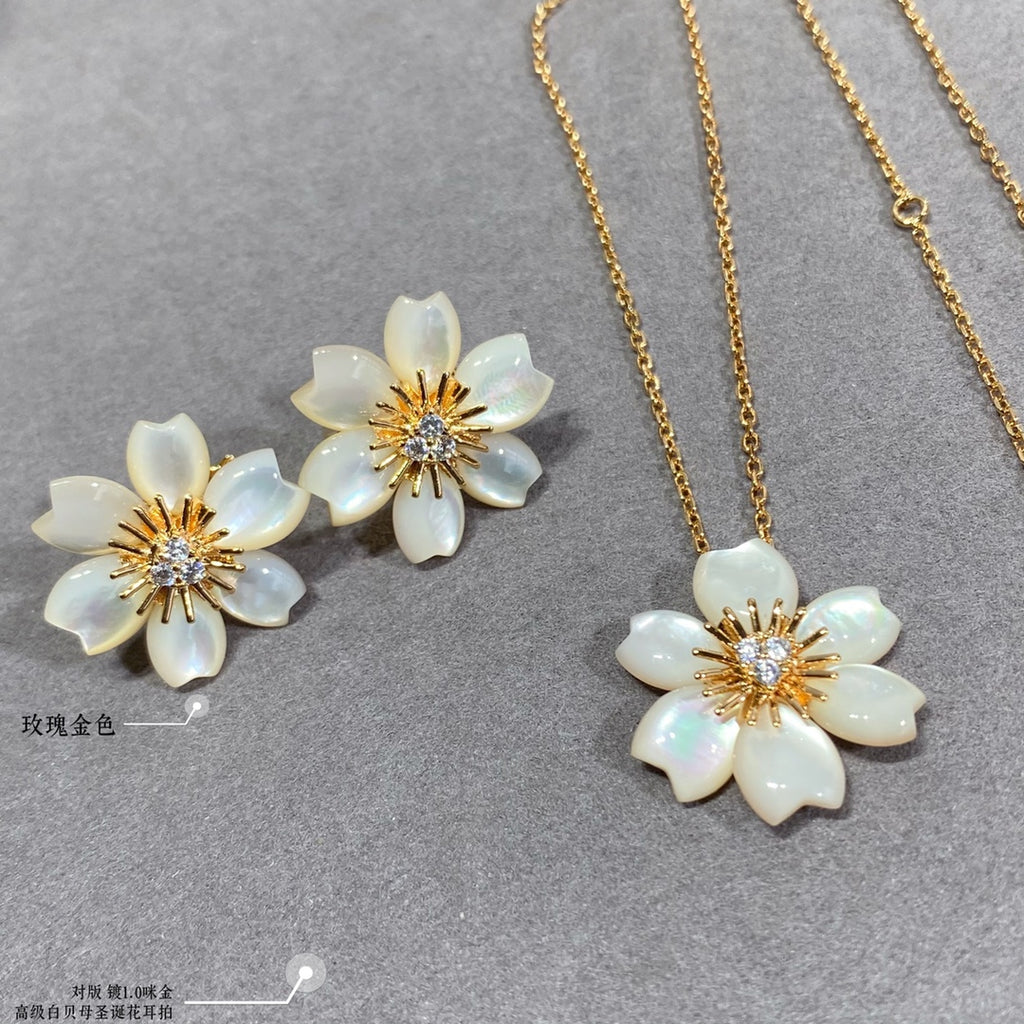 White flower stud earrings and gold chain necklace with white flower pendant on gray display