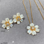 White flower stud earrings and gold chain necklace with white flower pendant on gray display