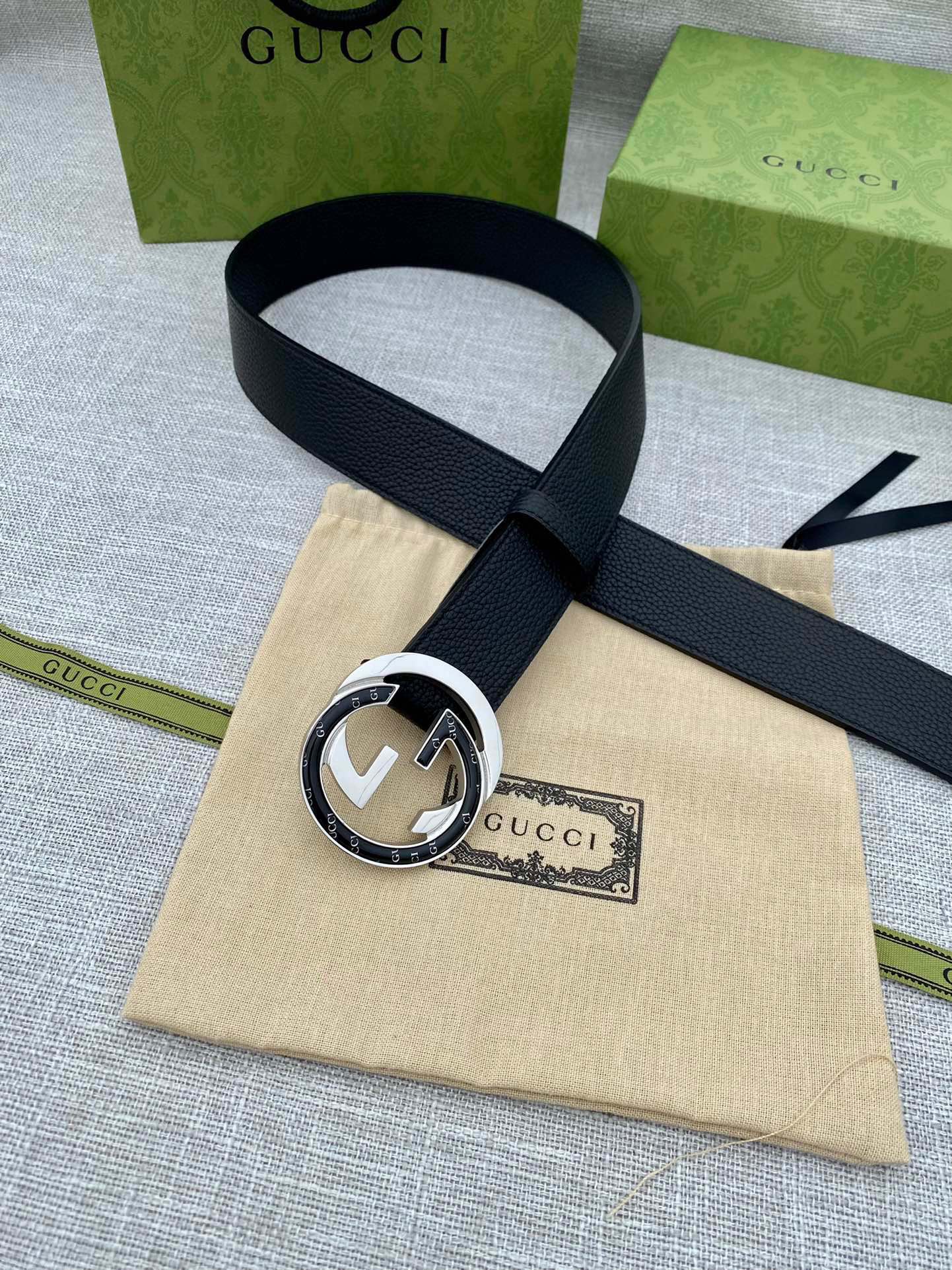 Black leather belt with silver-tone round double G buckle, laid across a pouch.