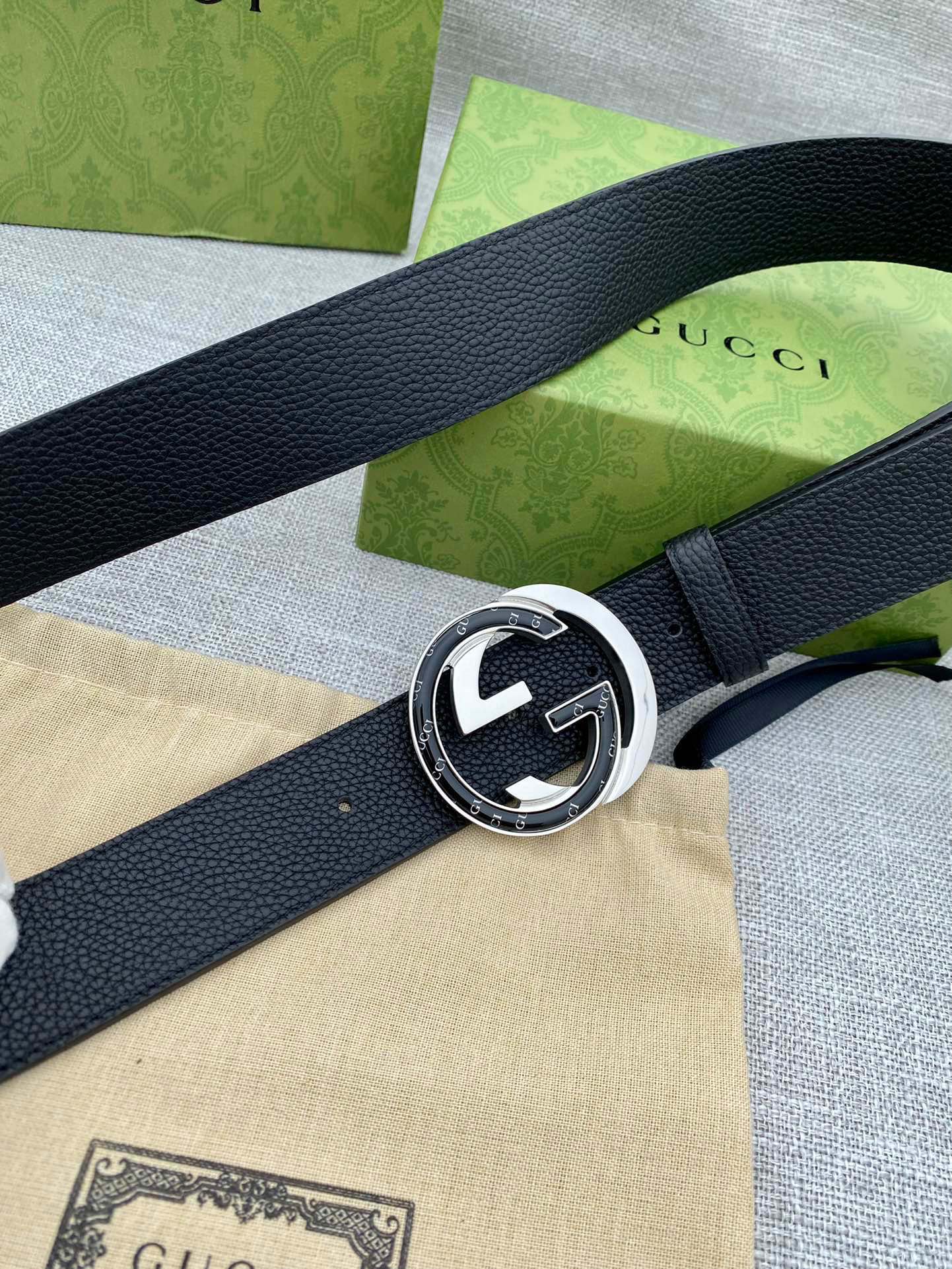 Black leather belt with silver-tone double G buckle on a curved strap close-up.