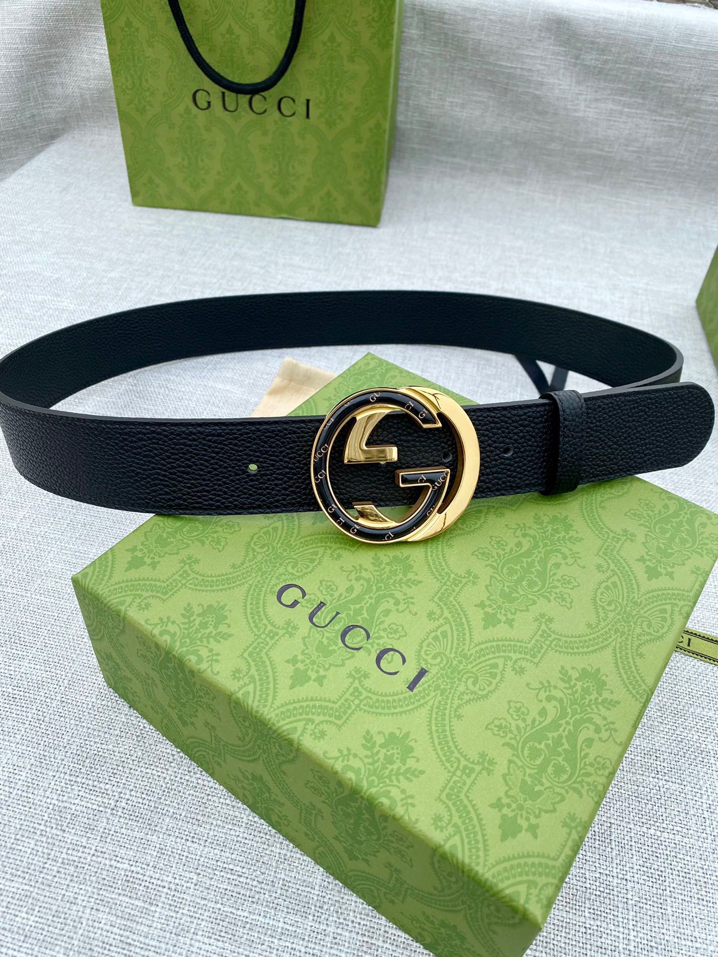 Black leather belt with gold-tone double G buckle and round center emblem.