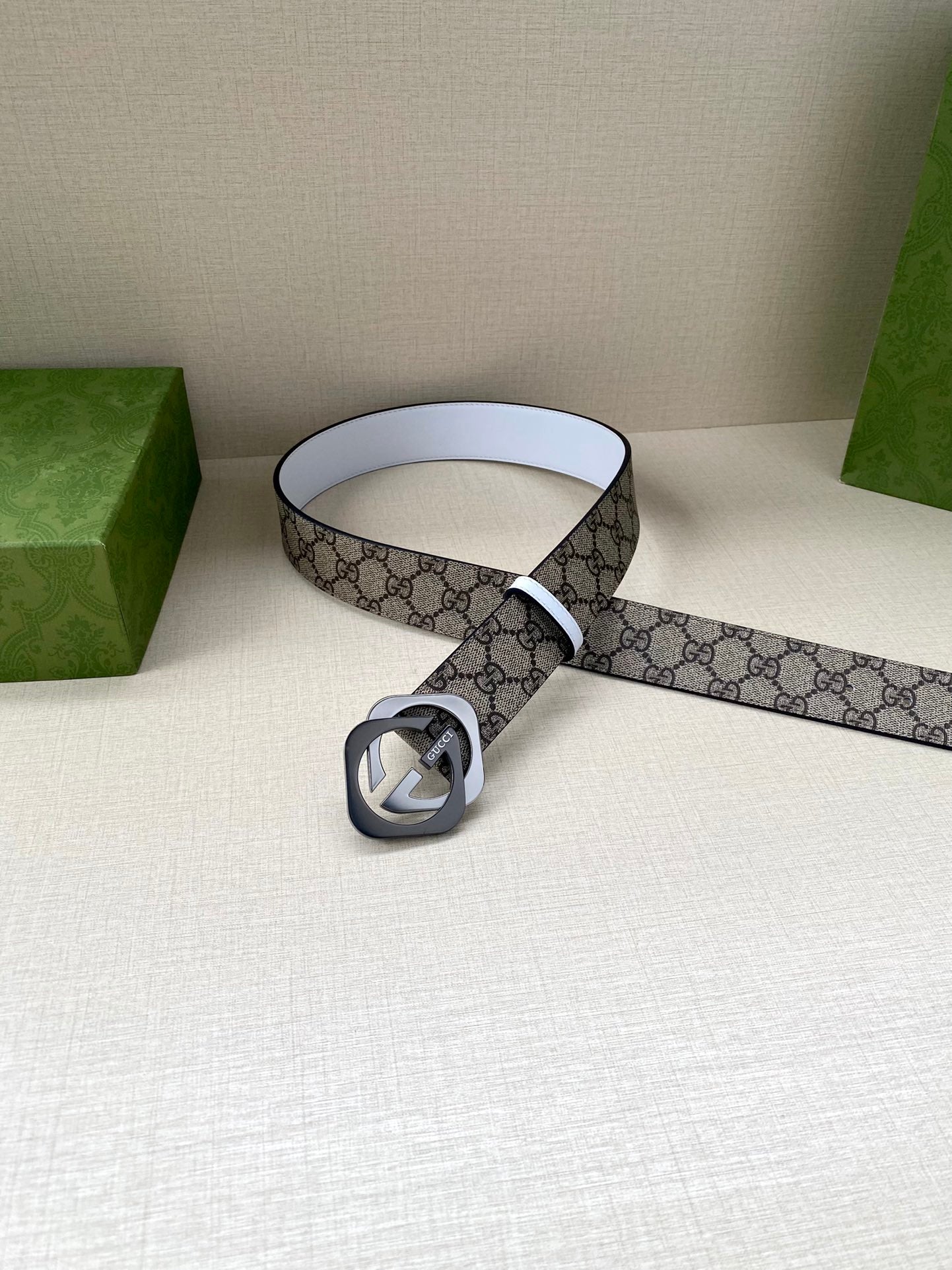 Gucci belt displayed coiled, beige-brown GG canvas strap with white edge and round interlocking G buckle