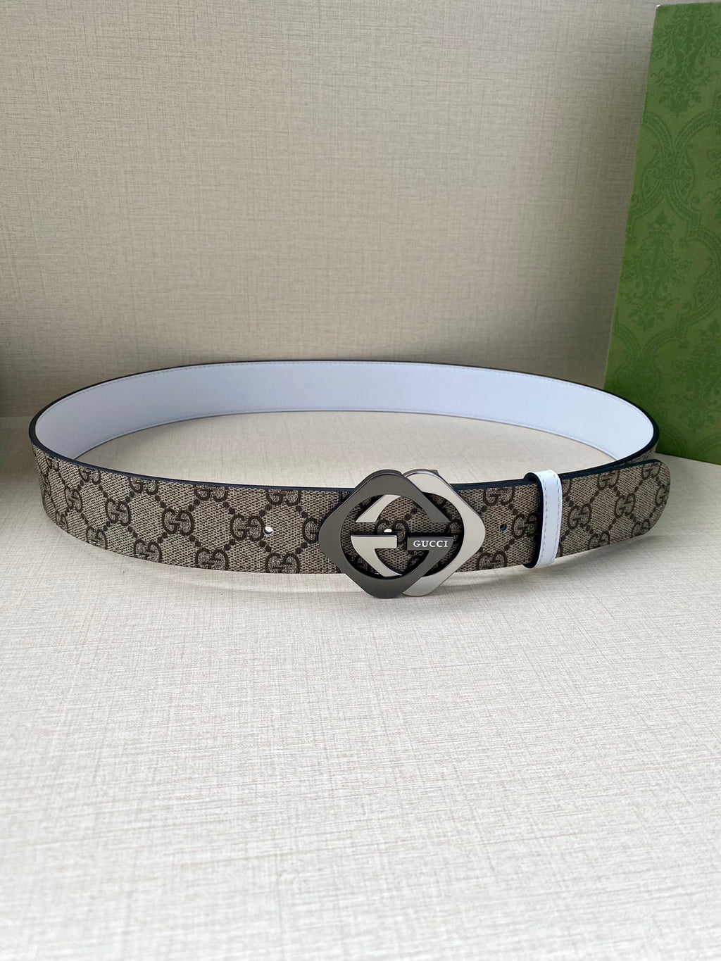 Gucci belt laying flat, beige-brown GG canvas with white edge and round interlocking G buckle