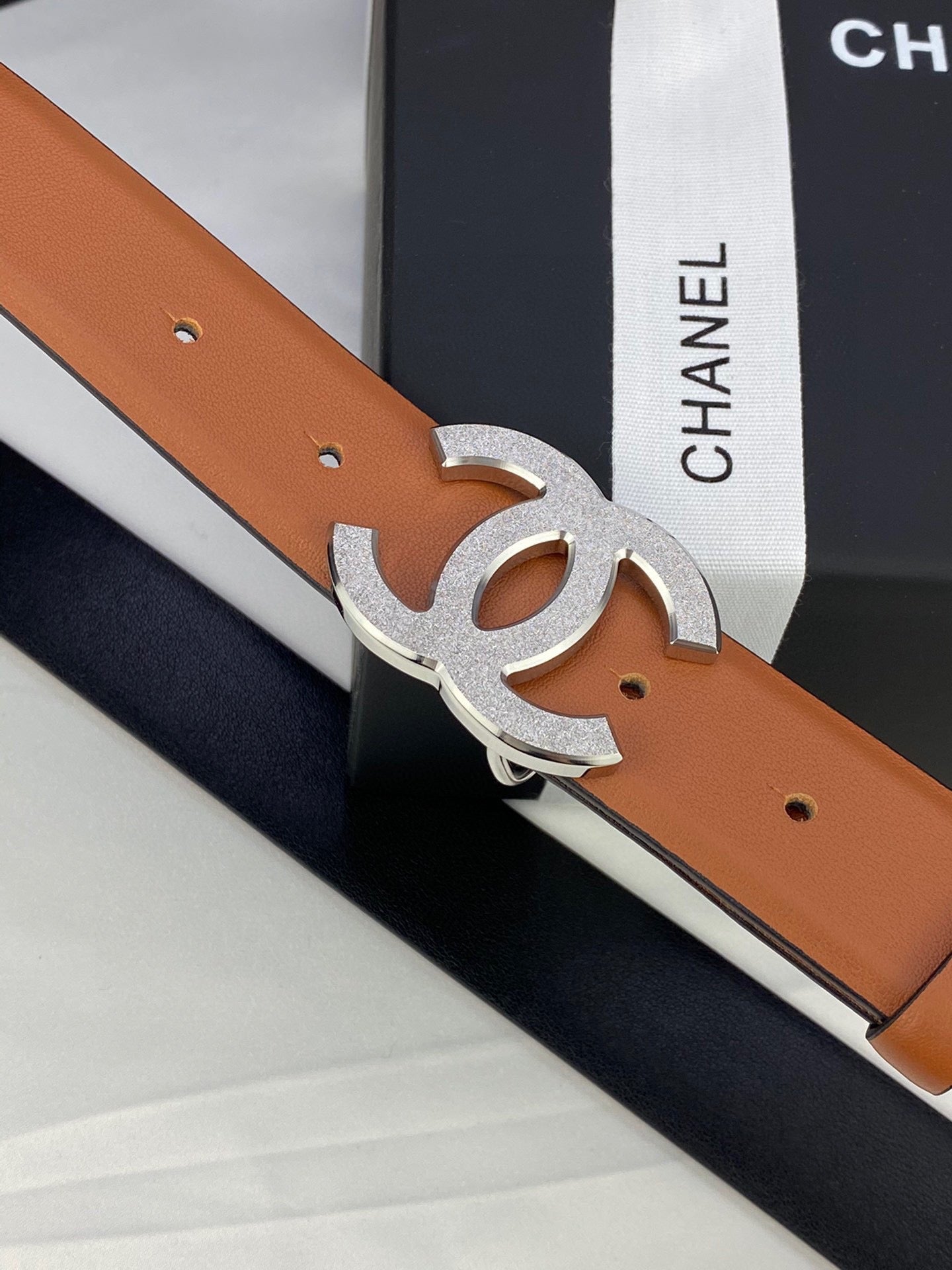 Tan leather belt with silver-tone CC buckle detail, close-up