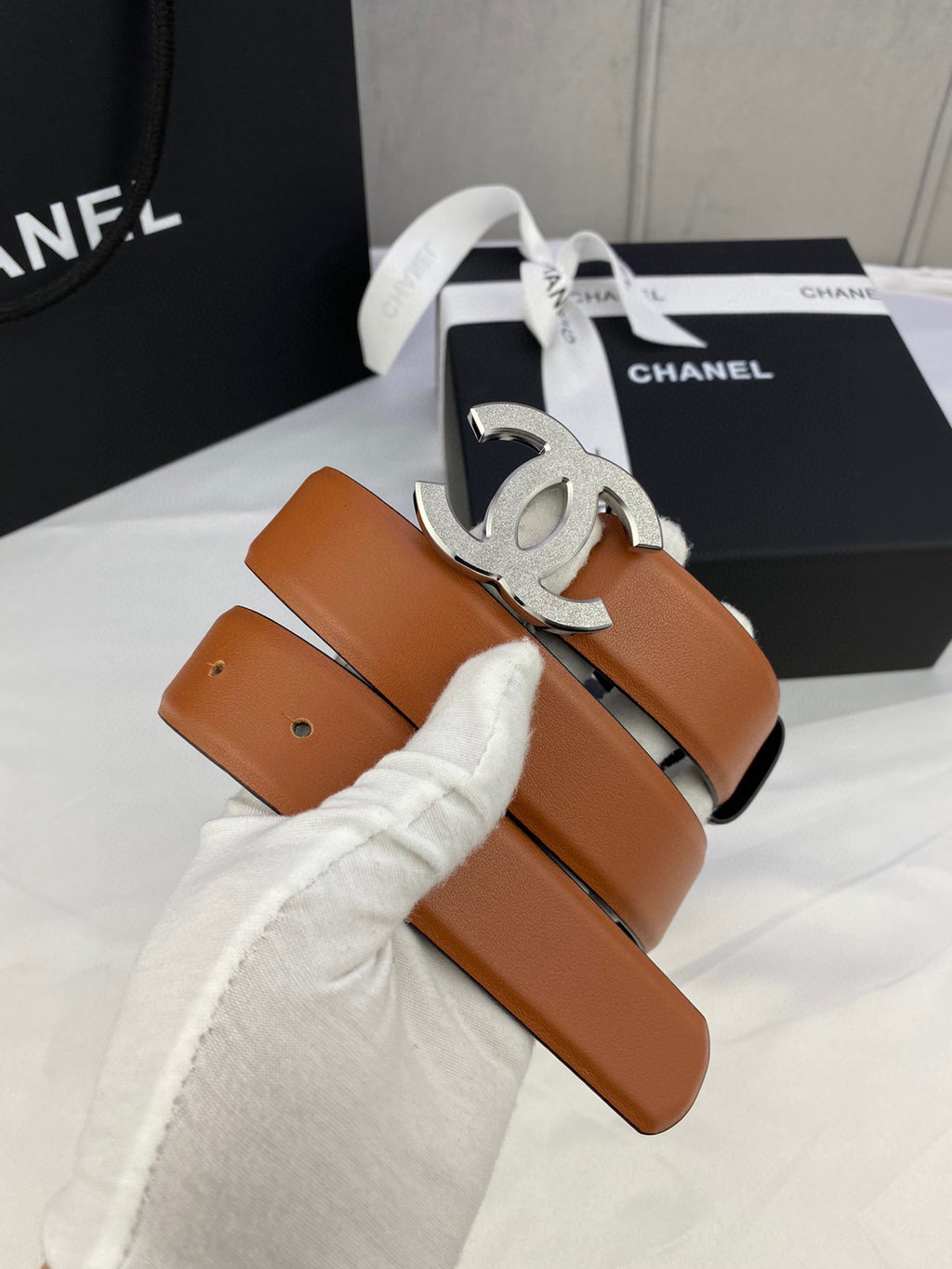 Tan leather belt with silver-tone CC buckle, coiled with folded white cloth and ribbon