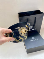 Hand holding navy Versace belt with gold pattern and round medallion buckle