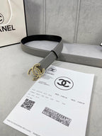 Chanel leather belt with gray strap and gold-tone CC logo buckle, laid across paper