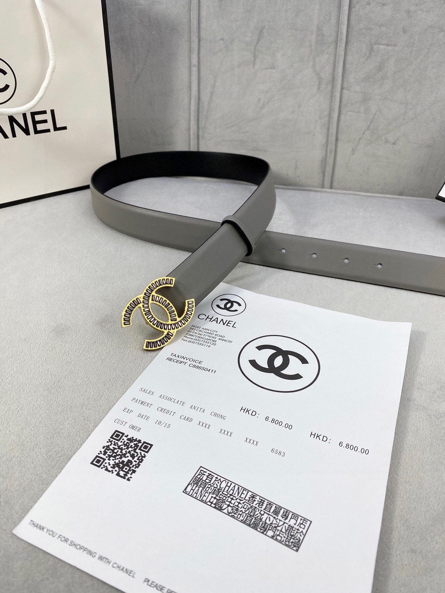 Chanel leather belt with gray strap and gold-tone CC logo buckle, laid across paper