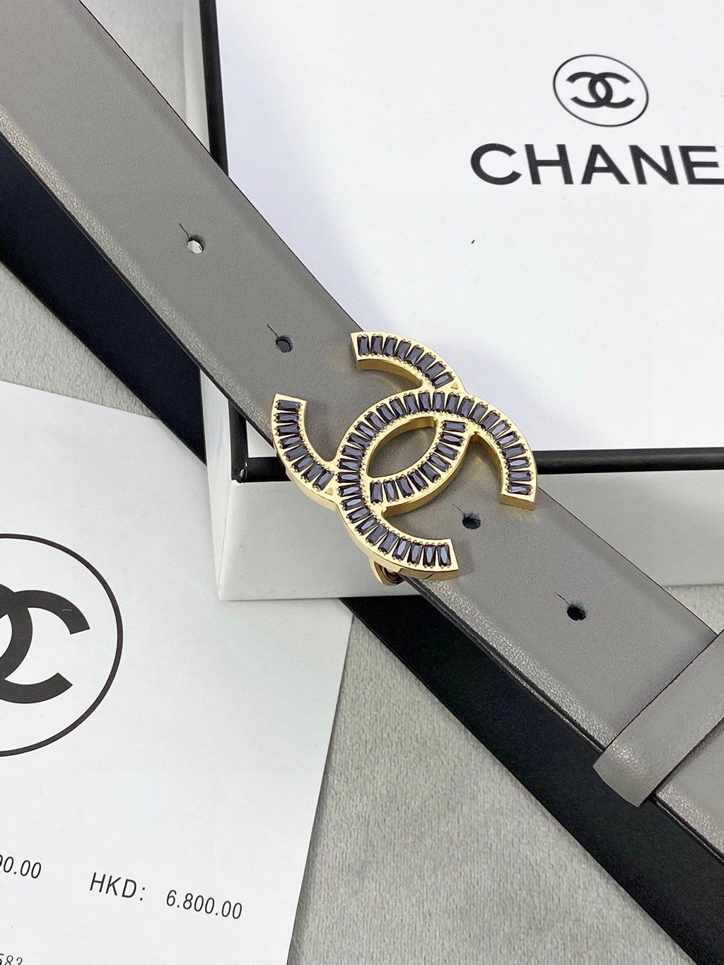 Chanel leather belt close-up: gray strap with gold-tone CC logo buckle and punch holes