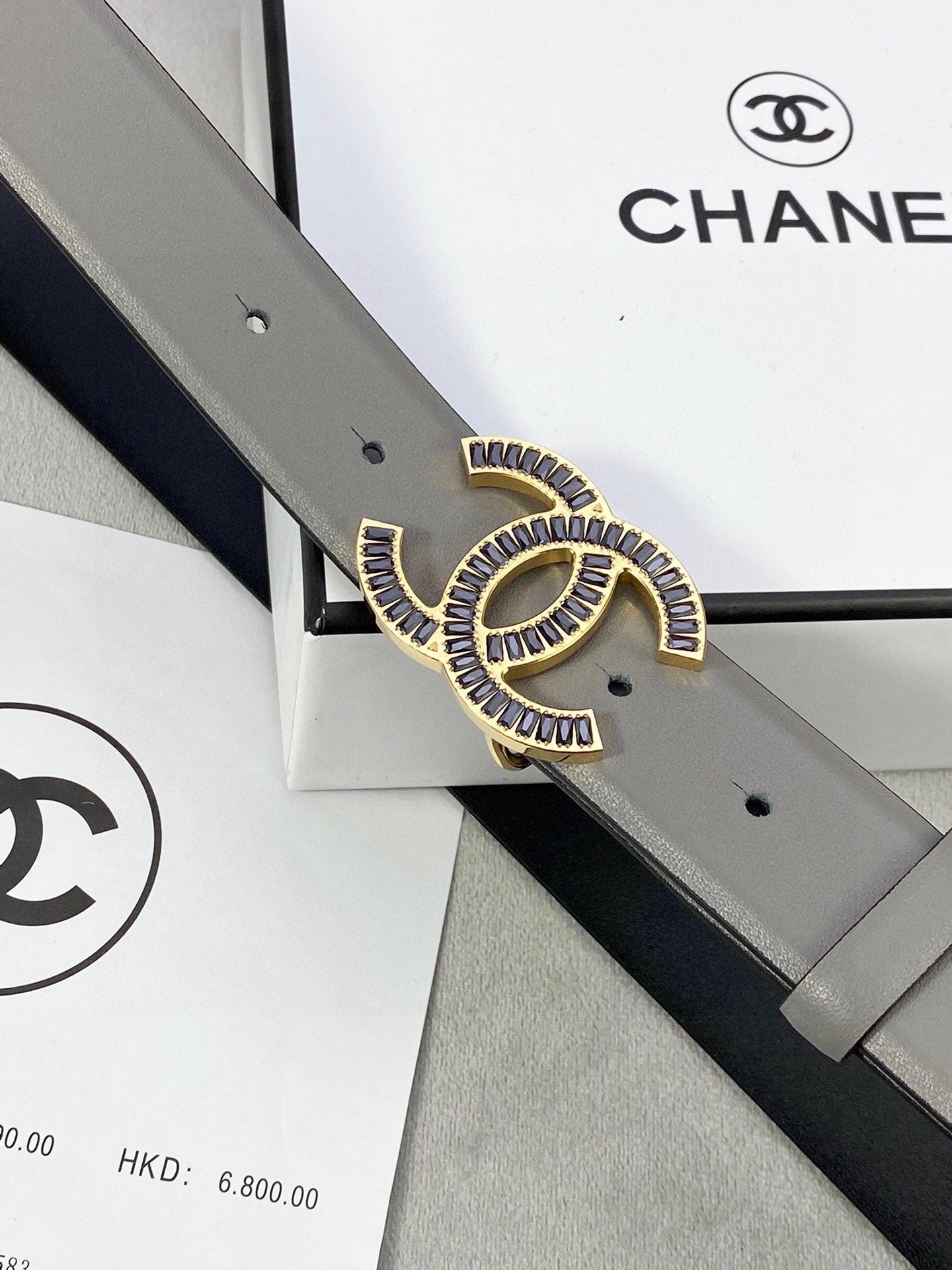 Chanel leather belt close-up: gray strap with gold-tone CC logo buckle and punch holes