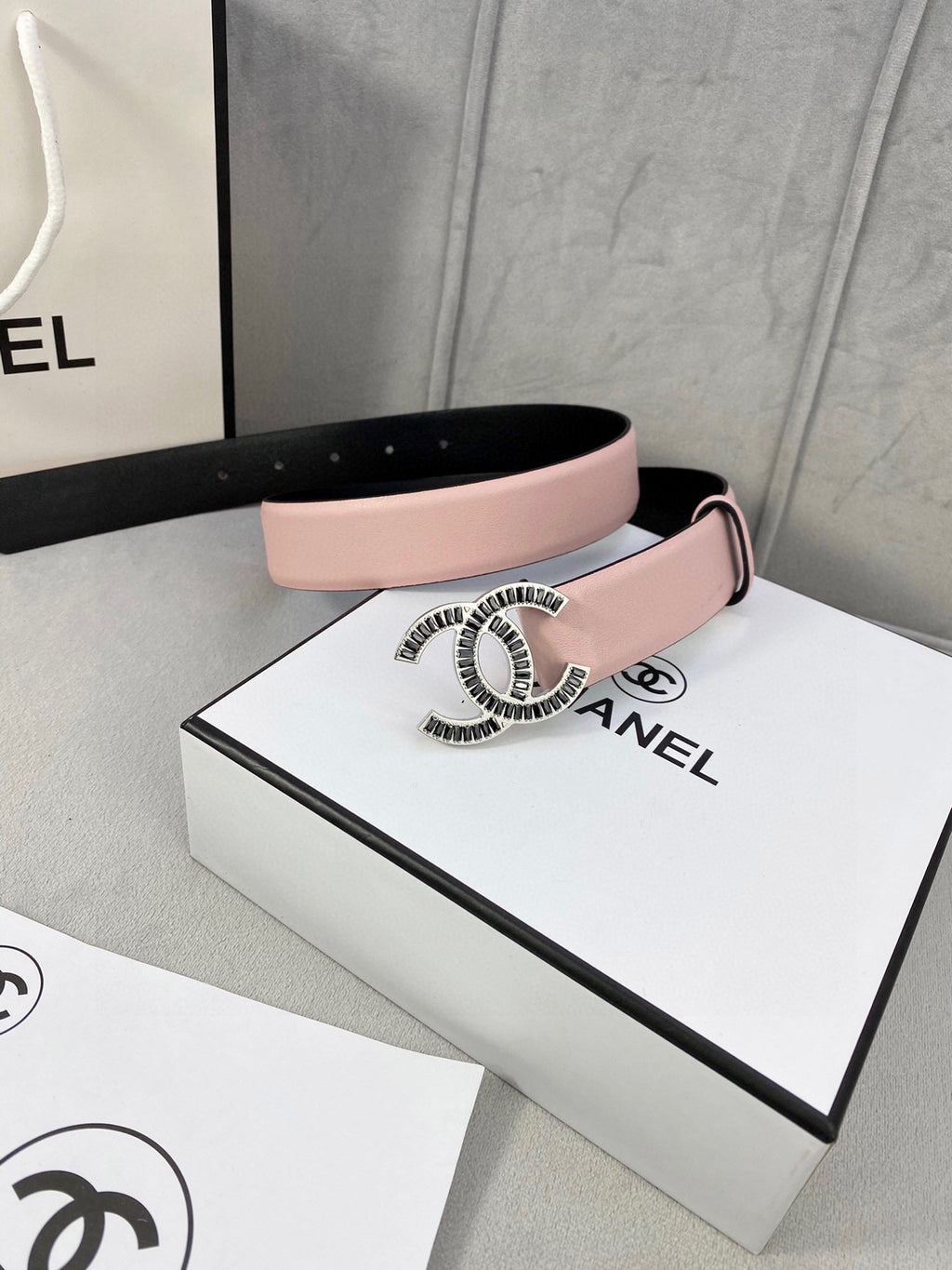Chanel belt with pale pink leather strap and gold logo buckle on a cream background