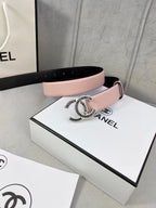 Chanel belt with pale pink leather strap and gold logo buckle on a cream background