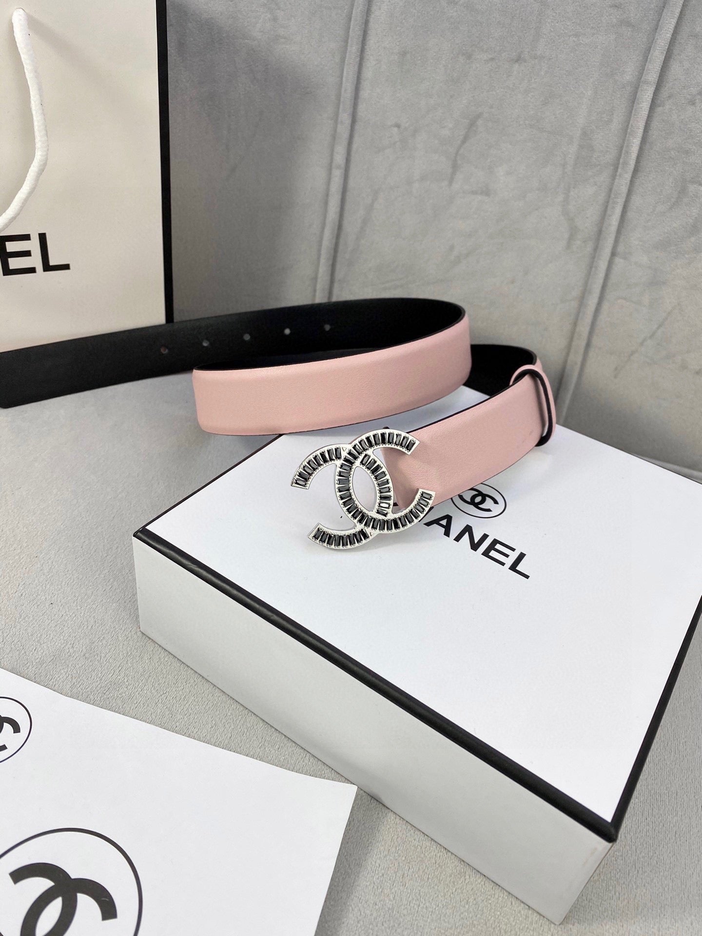 Chanel belt with pale pink leather strap and gold logo buckle on a cream background