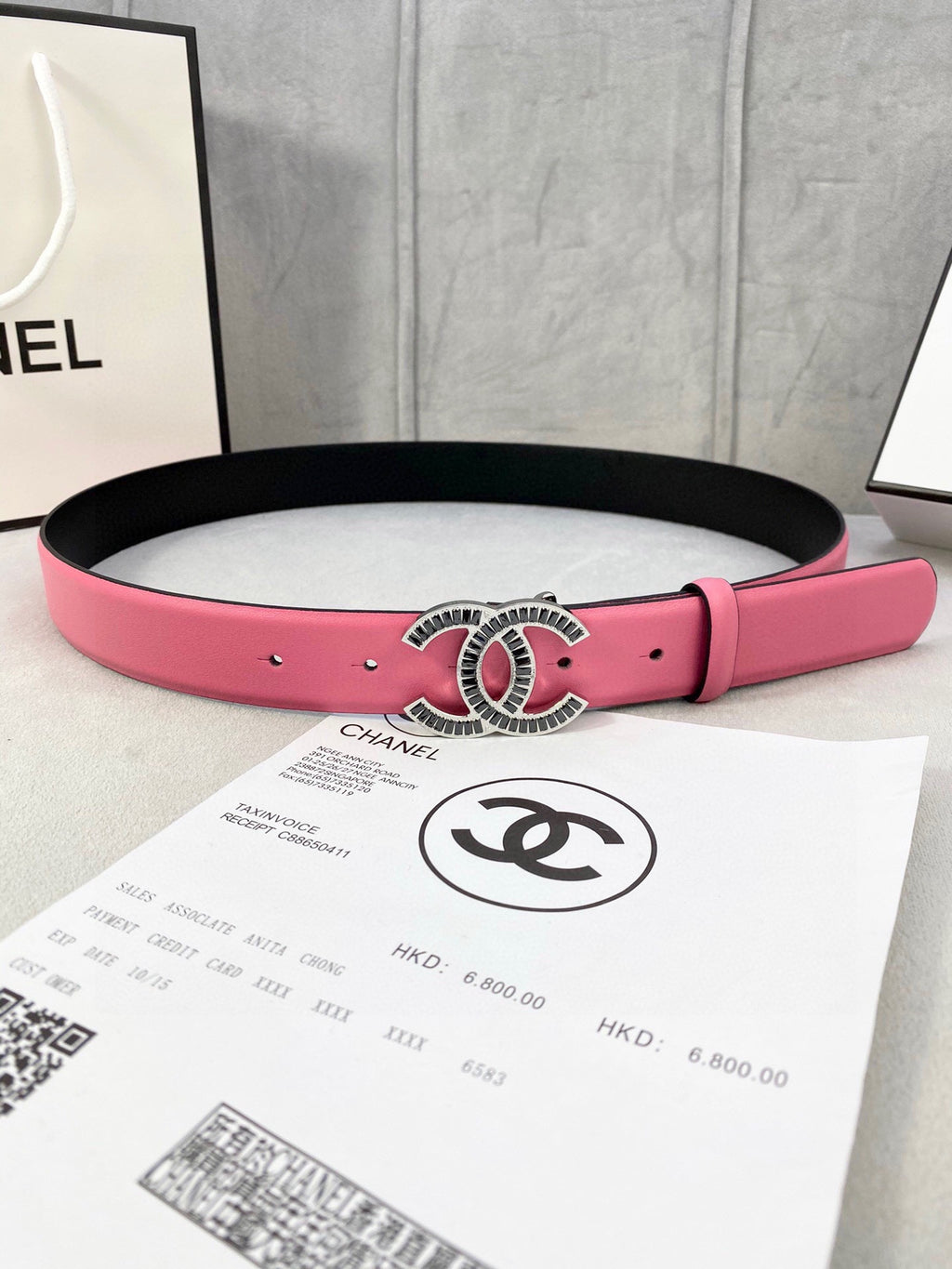 Chanel belt with pink leather strap and ornate oval CC buckle on black backing.
