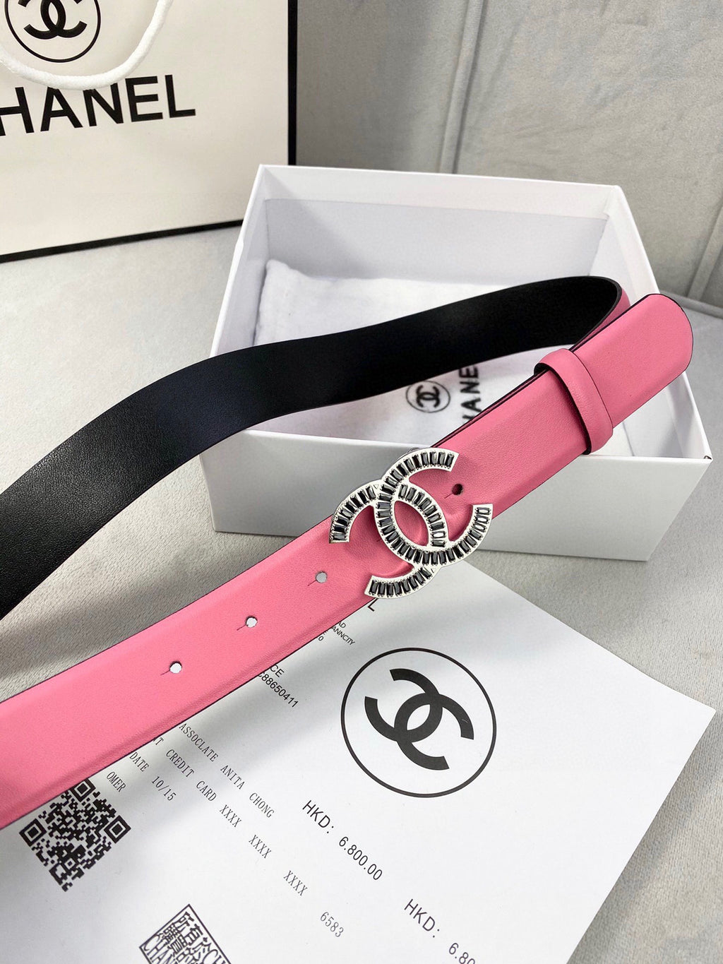 Chanel belt on box: pink strap with silver CC buckle featuring red center, black underside.